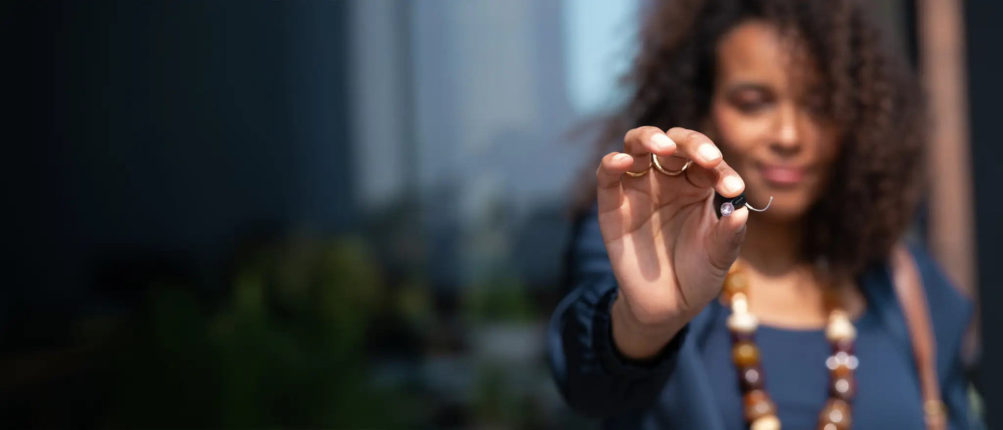A person holding the tiny Oticon Zeal in-the-ear hearing aid between two fingers